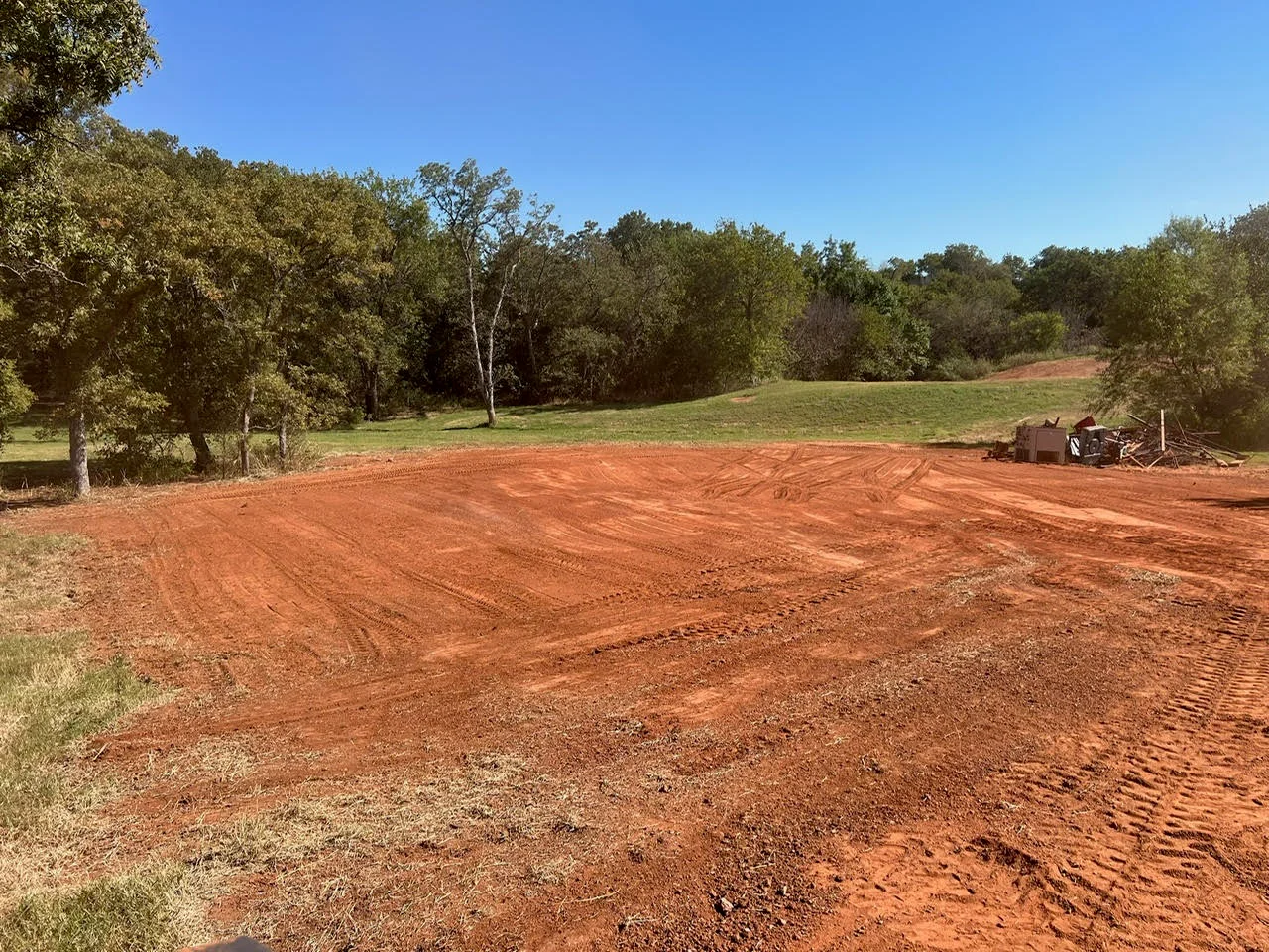 Freshly excavated and graded residential lot with red clay soil and mature trees