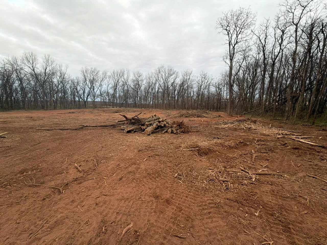 Cleared wooded lot with staged tree debris and bare earth in Lawton, OK