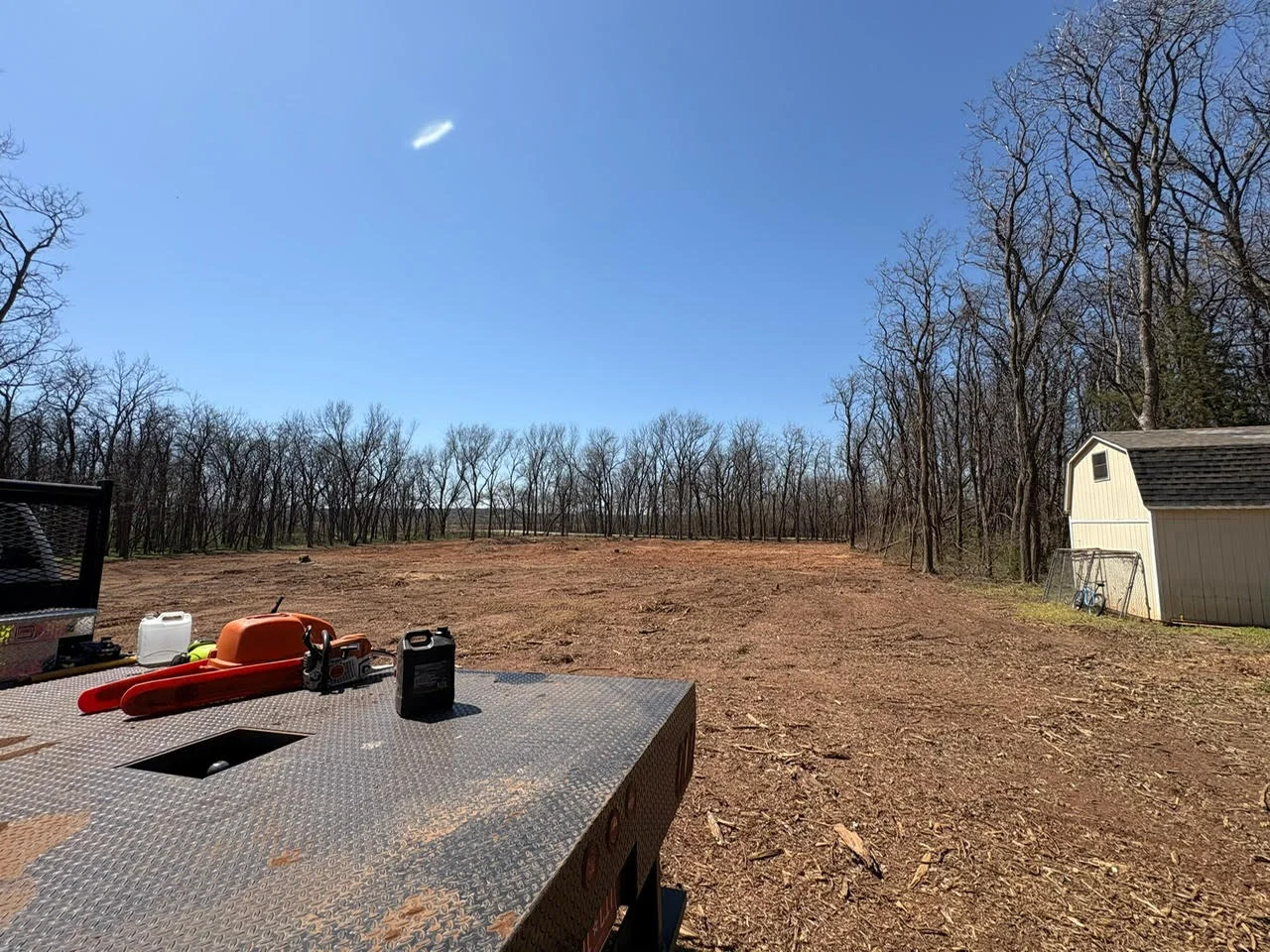 Cleared wooded lot with graded dirt surface, storage shed, and excavation equipment