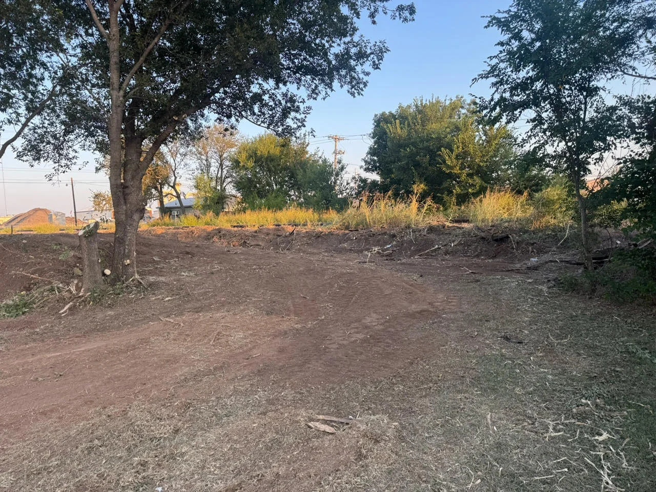 Cleared and graded residential lot with mature trees and prepared soil ready for construction