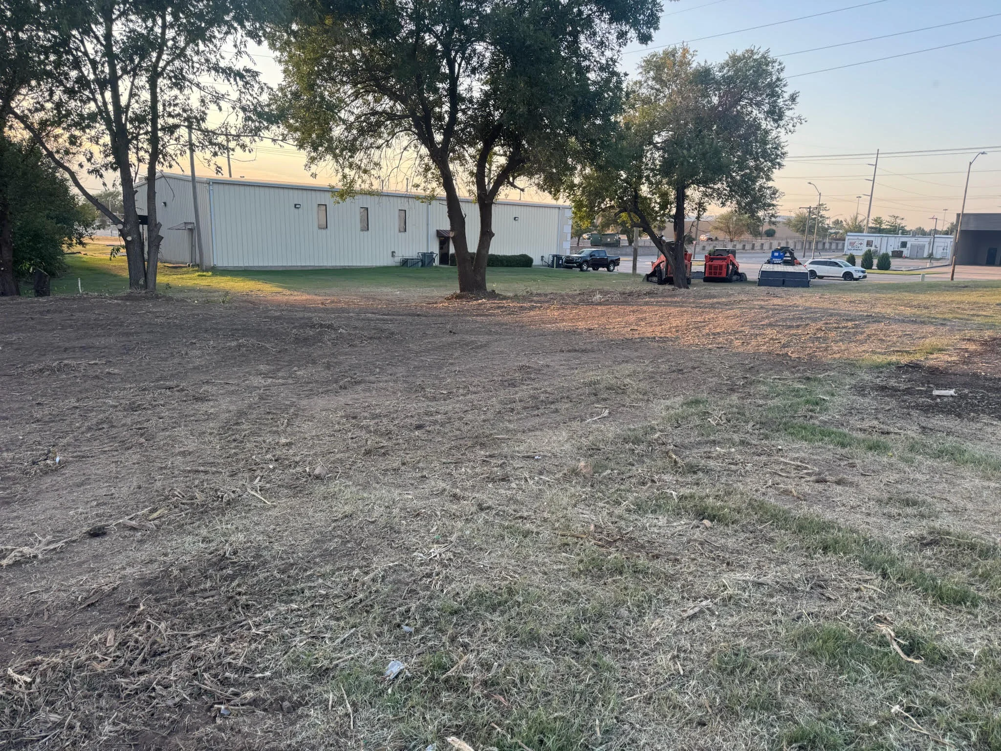 Cleared commercial lot with metal warehouse building and mature trees