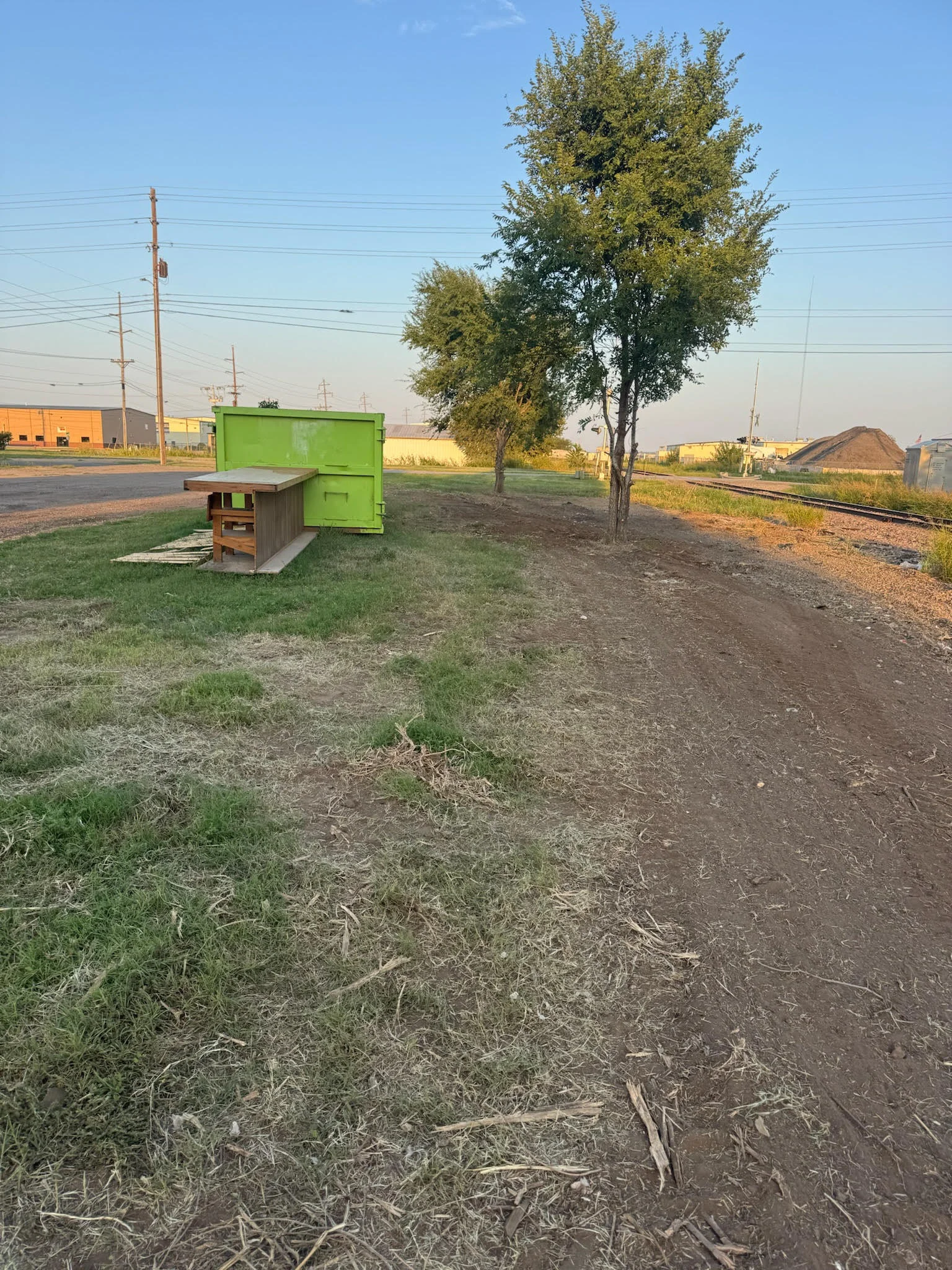 Cleared industrial lot with graded dirt, green storage container, and mature tree on property