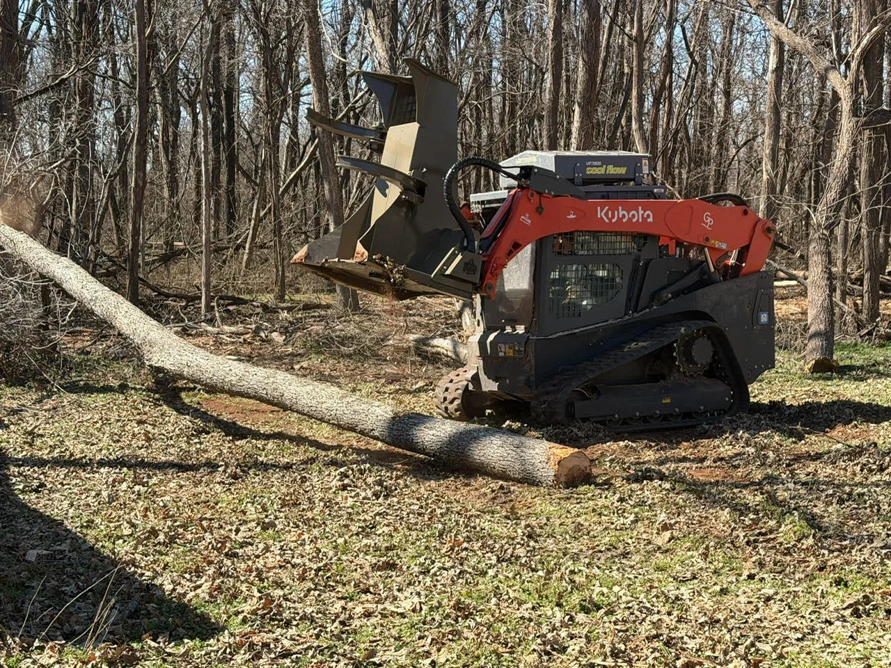 Red Kubota skid steer with wood chipper attachment processing logs in forest clearing