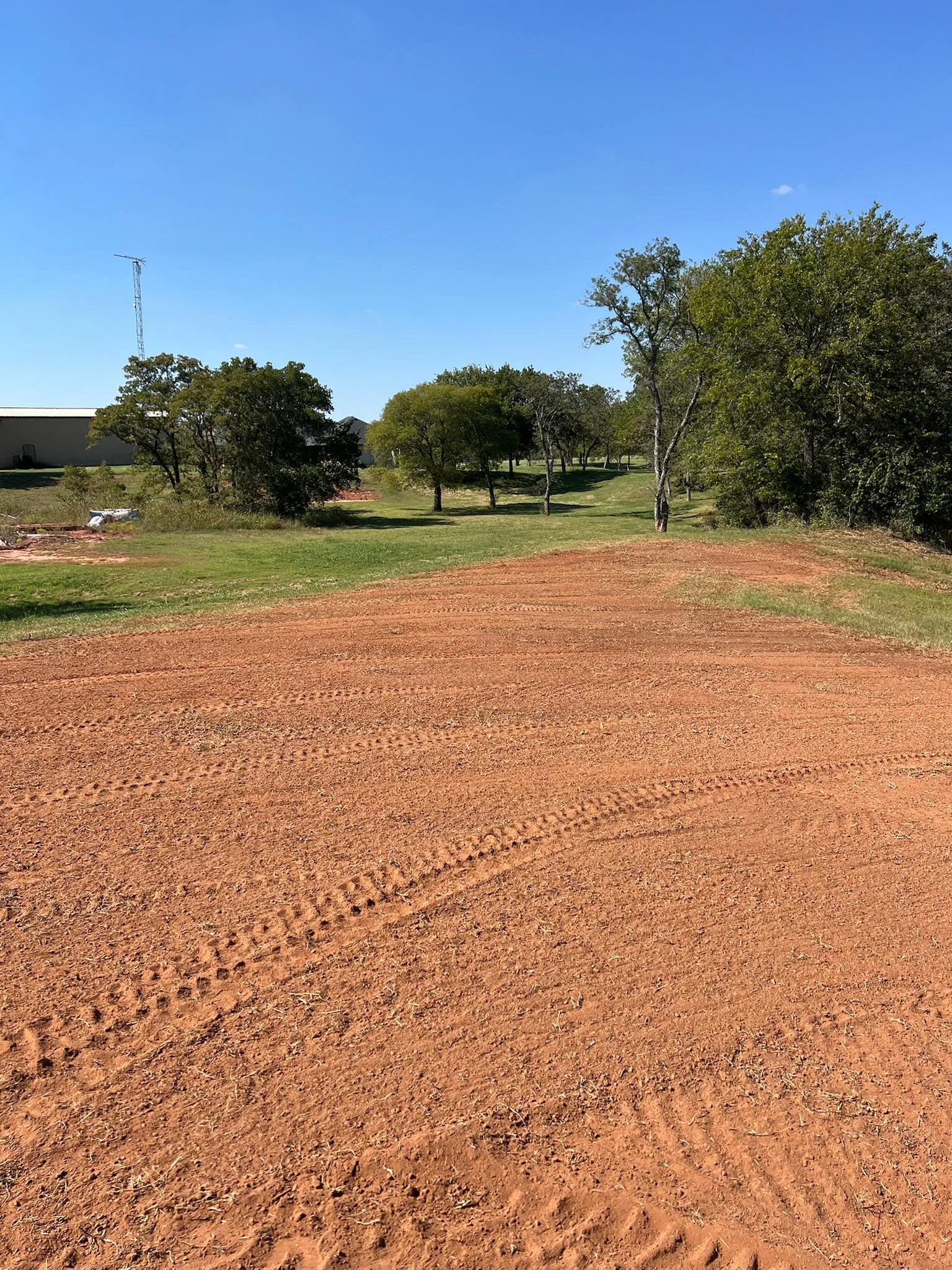 Newly graded red clay driveway with mature trees and cleared landscape in Lawton