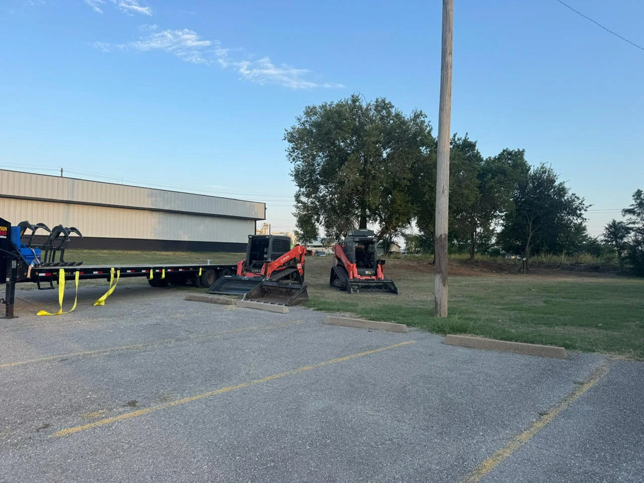 Two red compact track loaders and dump truck on graded commercial lot in Lawton