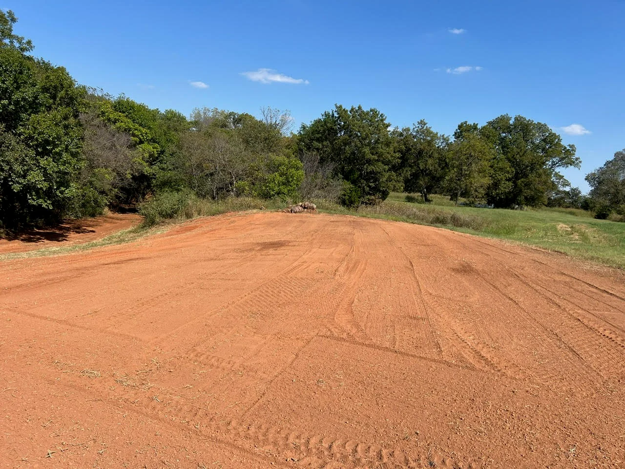 Freshly graded red clay driveway with tree-lined borders and clear grading marks